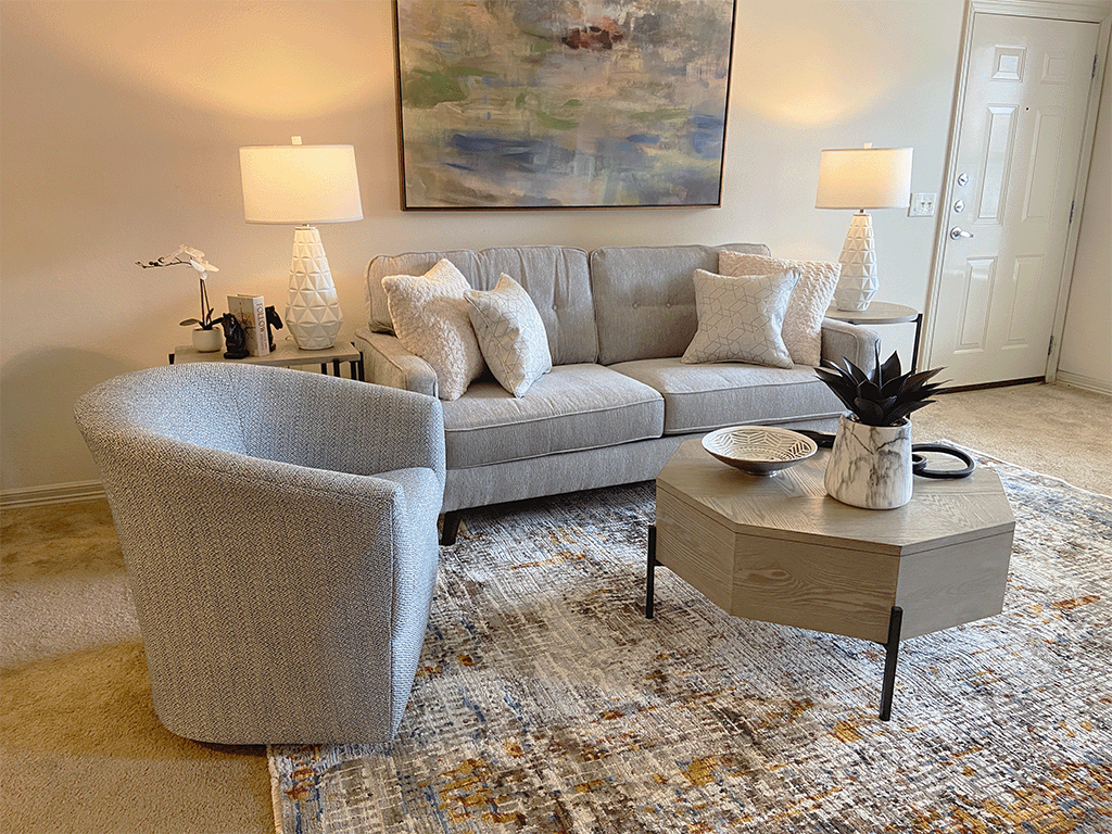 A grey couch with a grey chair and a table with a vase and a plant on it.